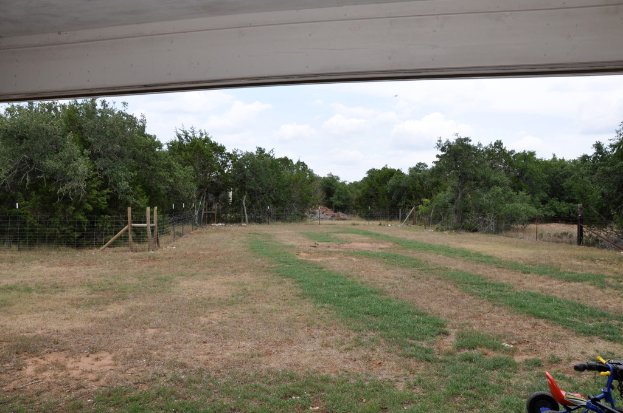 Eine offene grüne Wiese mit einem Zaun und Bäumen im Hintergrund und einem Fahrzeug auf der rechten Seite.
