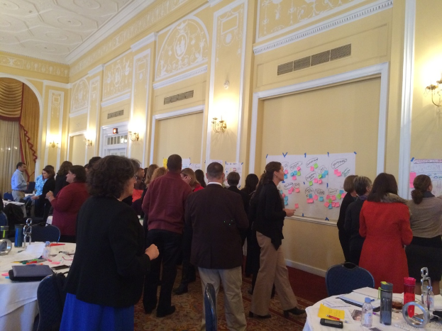 Eine Gruppe von Menschen betrachtet Plakate und Diagramme, die an einer Wand in einem scheinbar Kunstmuseum angebracht sind.