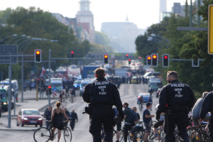 Polizeibeamte fahren mit Fahrrädern eine von Bäumen gesäumte Straße mit Gebäuden und einem klaren Himmel im Hintergrund.