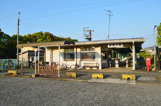 Ein Bahnhof mit Fahrrädern vorne, eine Straße unten und Häuser, Bäume, Pfähle, Drähte und einen klaren blauen Himmel im Hintergrund.