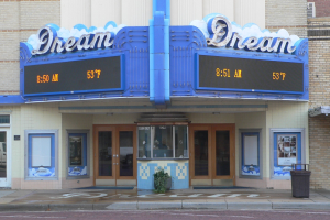 Außenansicht des Dream Theaters in St. Louis, Missouri, mit Glastüren und Fenstern, einem Namen auf dem Schild, einem Müllbehälter, einem Topf mit einer Pflanze und einer Straße unten.