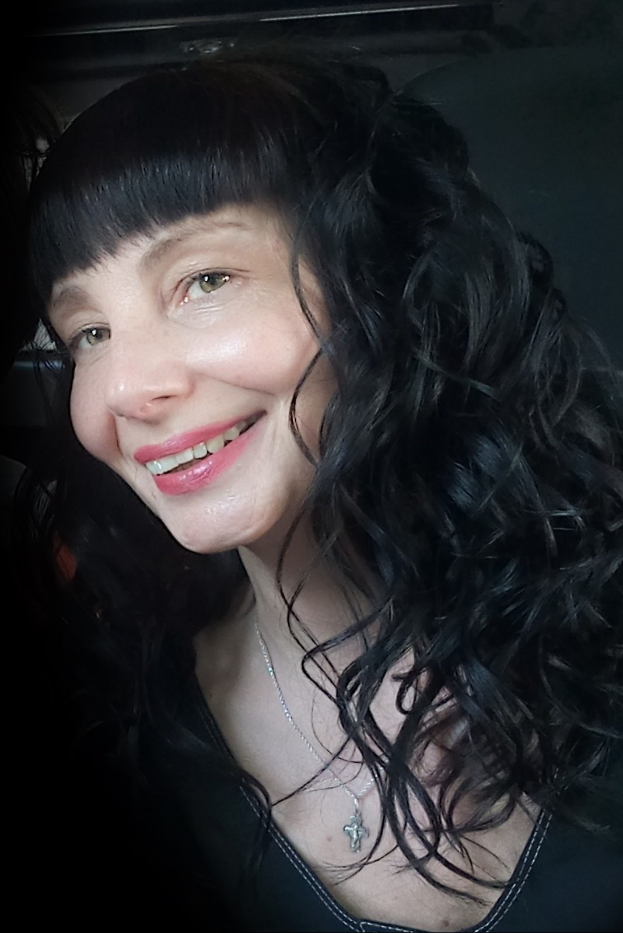 Eine strahlende Frau mit langen schwarzen Haaren und Pony, deren Gesicht von ihren Haaren umrahmt wird, mit einem warmen und fröhlichen Ausdruck.