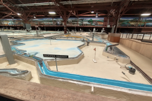 Indoor-Wasserpark mit mehreren Wasserrutschen, Deckenleuchten, Wandgemälden und einem Minigolfplatz.
