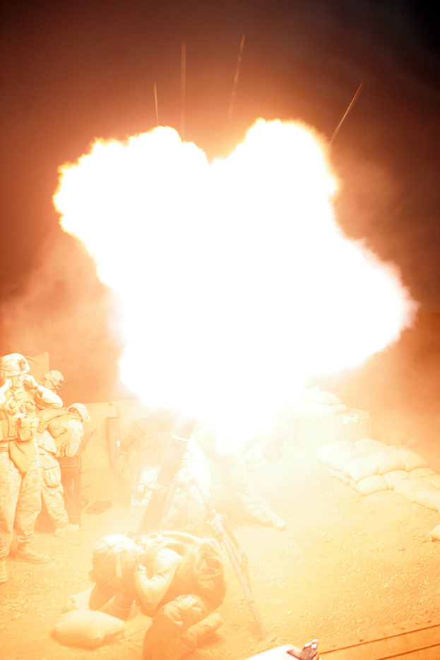 Mehrere Personen in Uniformen und Helmen befinden sich auf einem Gelände mit Taschen, wobei ein Feuer in der Mitte der Szene lodert.