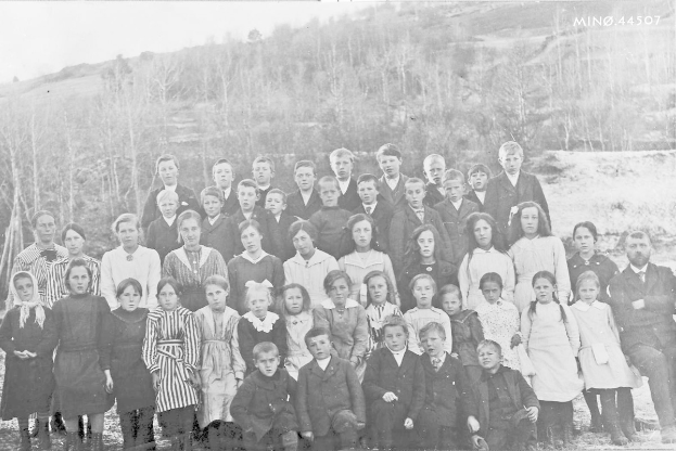 Ein Schwarz-Weiß-Foto einer Gruppe von Kindern, die vor Bäumen und einem Hügel posieren, mit dem Text "1930-1940 Schulkinder" unten.