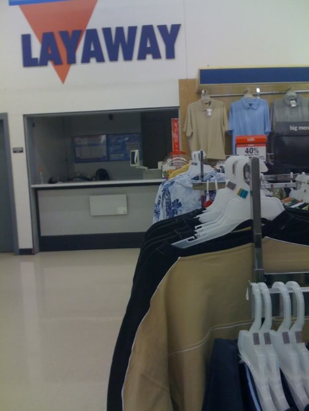 Ein Innenblick in ein Geschäft mit Kleidung an Bügeln, einem Tisch und einer Preistafel.