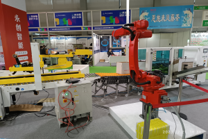 Eine Gruppe von Robotern auf einem Tisch umgeben von Maschinen und elektronischen Bauteilen in einer Fabrikumgebung mit ein paar Menschen im Hintergrund.