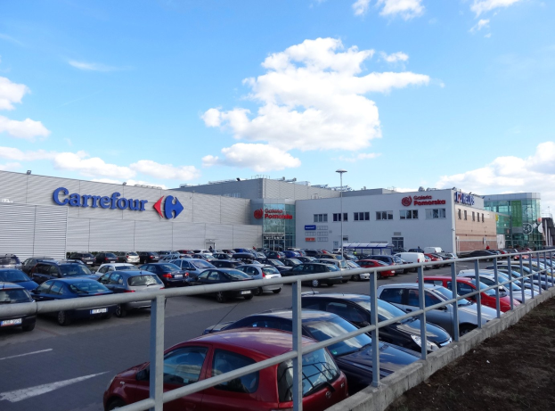 Großes Autohaus mit zahlreichen parkenden Fahrzeugen, umgeben von städtischen Gebäuden, Straßeninfrastruktur und Fahrzeugen auf der Straße.