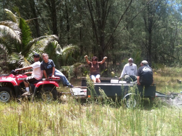 Eine Gruppe von Menschen auf einem Traktor sitzend, mit einer Person, die es fährt, und Bäumen im Hintergrund.