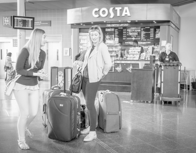 Zwei Frauen mit Gepäck vor einem Kaffeehaus an einem Ort, der wie ein Flughafen aussieht.