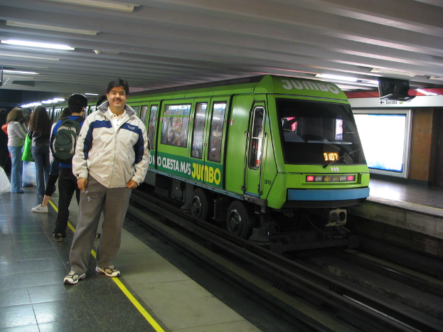Ein Zug auf Eisenbahnschienen mit Menschen, die links stehen und ein Dach oben im Bild.