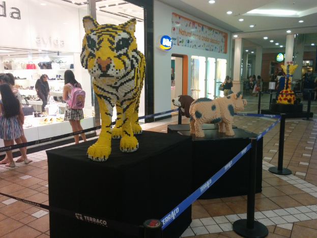 Statuen von Tieren auf schwarzen Boxen umgeben von Pfählen mit Gummibändern, mit Geschäften, die Taschen, Schuhe und andere Gegenstände anbieten, und Menschen, die herumlaufen.