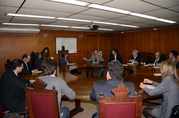 Mehrere Personen sitzen um einen runden Tisch mit einer Wandkarte im Hintergrund.