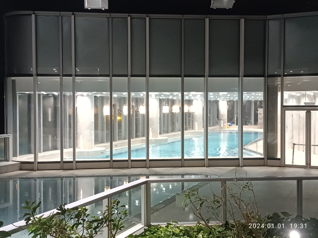 Ein großes Hallenbad in einem Dubai-Hotel, umgeben von Glaswänden und beleuchtet von Deckenlampen, mit Pflanzen und einem Geländer am Boden.