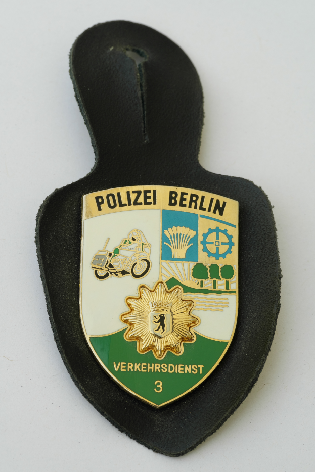 Ein Polizeistern mit blauem Hintergrund, weißer Stern und weißem Rand, auf dem der Text 'Polizei Berlin' in fetter schwarzer Schrift steht.