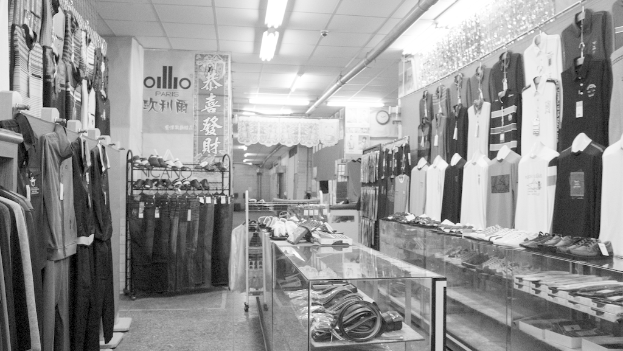 Eine Anzeige von Kleidung, Gürteln und Schuhen mit einer Uhr an der Wand, hängendem Stoff, Lichtern und einem Banner mit Text auf der linken Seite.